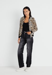 Leopard print bomber jacket with black ribbed cuffs, paired with dark denim jeans and white sneakers. Model stands against a plain background.