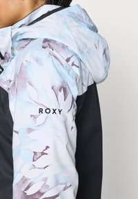 Daudzkrāsaina jaka ar gaiši zilu un violetu ziedu rakstu kapucē un plecos, tumši pelēku ķermeni un "ROXY" logotipu.