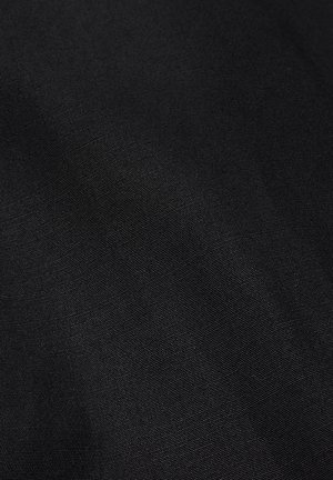 Gros plan sur un tissu noir texturé avec un motif fin tissé, montrant des variations subtiles de lumière et d'ombre.