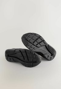 Baskets noires avec des semelles en caoutchouc texturé, dotées de motifs de semelle multidirectionnels et d'un renfort au talon pour une meilleure adhérence et durabilité.