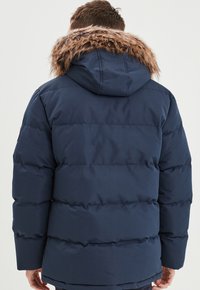 Marineblaue Daunenjacke mit Kapuze und Kunstfellbesatz, ausgestattet mit genähten Bereichen für Isolierung und einer glatten Stoffoberfläche.