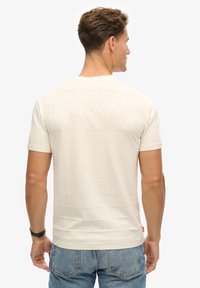 Camiseta de color crema claro con rayas horizontales, de manga corta, con cuello redondo, fabricada con una suave mezcla de algodón, combinada con jeans de mezclilla azules.