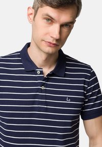 Granatowa koszulka polo w białe poziome paski, z trzema guzikami, krótkimi rękawami oraz logo na lewej piersi. Tekstura z bawełnianego materiału.