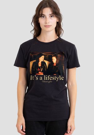 Young woman wearing black t-shirt with a "Gilmore Girls" print showing two women sitting and the text "It's a lifestyle."