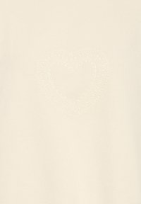Tissu crème avec une forme de cœur subtile et texturée composée de petits points en relief centrée sur la surface.