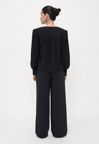 Blusa nera con scollatura ampia e maniche a sbuffo, con dettagli di bottoni sui polsini, abbinata a pantaloni neri a vita alta.