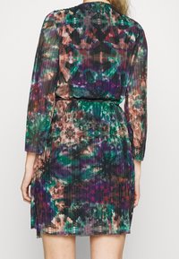 Plisse dress in multicolored fabric featuring green, purple, and orange patterns. Long sleeves and a tie belt at the waist. Lightweight texture.