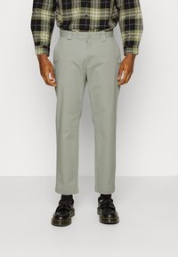 Light green cotton trousers with a straight-leg design, featuring side pockets and a belt looped waistband. Worn with black shoes.