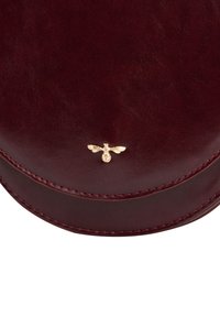 Smooth dark red leather bag with curved flap, detailed stitching, and small gold bee emblem centered on the flap.