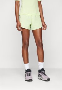 Lys grønn trening shorts og matchende topp, kombinert med lilla og svarte joggesko. Stoffet ser lett og teksturert ut.