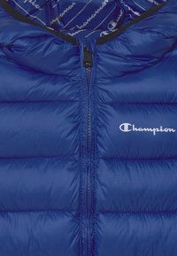 Blå puffer väst med en slät, glänsande yta, med hög krage, full dragkedja och "Champion"-logotypen i vitt på framsidan.