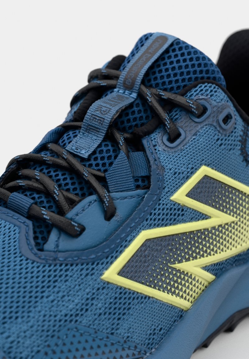 Chaussure de sport bleue avec tige en mesh respirant, superpositions en synthétique texturé, lacets noirs et un logo géométrique jaune distinctif.