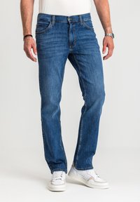 Dżinsy denimowe w średnim niebieskim odcieniu, posiadające pięć kieszeni, prosty krój nogawek oraz subtelne przetarcia. Połączone z białymi trampkami.