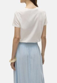 T-shirt blanc à manches courtes avec un col rond, associé à une jupe bleu clair avec une taille smockée. La texture semble douce et lisse.