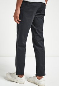 Chinos azul oscuro hechos de algodón, con un corte recto, bolsillos laterales y una textura suave, combinados con zapatillas blancas.