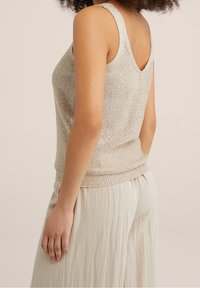 Ärmlös, ljusguldig stickad linne med en texturerad yta och ribbat nederkant, bärs med lösa, krämfärgade byxor.