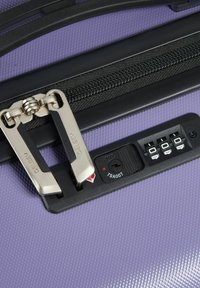 Valigia rigida viola con superficie texturizzata, dotata di una zip nera, meccanismo di doppia chiusura e lucchetto a combinazione approvato dalla TSA.