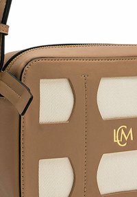 Sac bandoulière en cuir marron avec des accents en toile crème, logo doré, forme rectangulaire et fermeture éclair. Présente une texture contrastante et des coutures visibles.