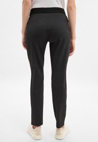 Schwarze gemusterte Hose mit einem strukturierten Zickzackdesign, ausgestattet mit einem breiten elastischen Bund und slim fit, kombiniert mit hellen Sneakers.