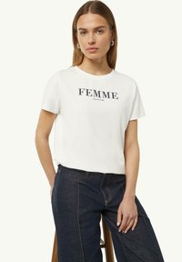 Witte katoenen t-shirt met korte mouwen, met marineblauwe tekst "FEMME" en "comma." Ronde halslijn, relaxte pasvorm, gecombineerd met donkere denim broeken.