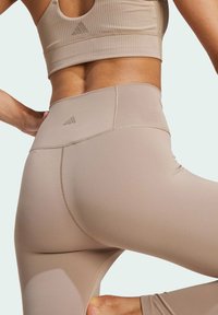 Beżowe legginsy sportowe z wysokim stanem i dopasowanym krojem. Posiadają płaskie szwy oraz wytłoczone logo z tyłu. Gładka faktura.