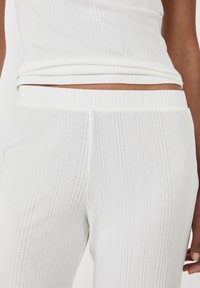 Conjunto de top y pantalones de tejido blanco acanalado, que presenta un diseño ajustado, una superficie texturizada y una cinturilla y dobladillo a juego para un estilo sin costuras.