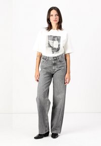 Tricou alb cu imprimeu grafic, asortat cu blugi gri, cu talie înaltă și croială largă, și botine negre. Design simplu și croială modernă.