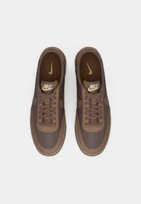 Pair of brown Nike sneakers with laces, beige swoosh logos on insoles, and beige Nike tags on tongues, seen from above on a white background.