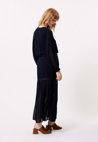 Marineblauwe maxijurk met polkadots, lange mouwen, een gelaagde rok en semi-doorzichte stof; gecombineerd met bruine open teen block-heeled sandalen.
