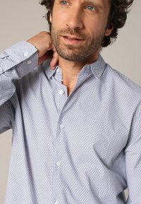 Witte overhemd met knopen, voorzien van een geometrisch patroon in marineblauw, met een puntkraag en textuurstof, gedragen door een persoon.