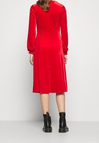 Röd sammetsklänning med långa ärmar, knälång fåll och åtsittande liv. Matchad med svarta ankelstövlar med kraftiga sulor.