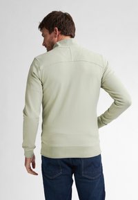 Pulover de culoare verde deschis, cu guler înalt, mâneci lungi și manșete cu dantelă. Textură netedă și detalii de cusătură pe partea superioară a spatelui.