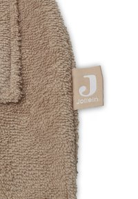 Tissu textile beige avec une surface texturée et duveteuse, accompagné d'une petite étiquette de marque Jollein, arborant un logo blanc sur un fond beige.