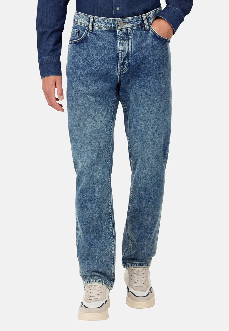 Šviesiai mėlynos džinsinės kelnės su tiesiu kirpimu, penkiais kišeniais ir subtiliu blukimu. Dėvimos su baltais sportbačiais, akcentuotais mėlyna spalva.