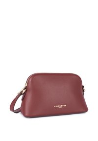 Borsa a spalla in pelle rossa con finitura текстurizzata, chiusura con zip e dettagli in oro. Presenta l'etichetta impressa "LANCASTER PARIS".