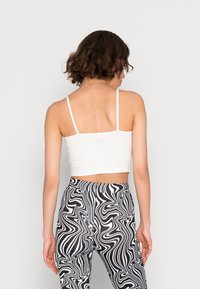 Top cropped branco ajustado com alças finas, combinado com leggings pretas e brancas com padrão ondulado. Textura suave, design minimalista.