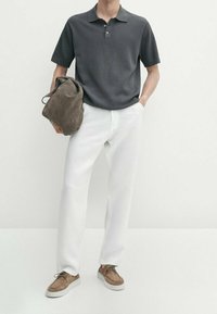 Polo shirt grigio scuro a maniche corte, pantaloni bianchi, sneakers beige e una borsa marrone, dalla texture morbida. Design semplice, colori neutri.