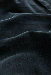 Donker denim stof met een zachte textuur en subtiele glans. Bevat gladde golven en plooien die de buigzame structuur en rijke kleur benadrukken.