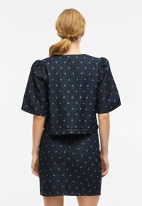 Robe en denim avec un tissu bleu foncé, ornée de pois bleu clair. Manches courtes bouffantes et silhouette ajustée. Ourlet net.