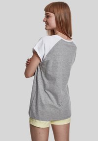 Grå og hvid kortærmet T-shirt med raglan-design. Blødt bomuldsstof, afslappet pasform, buet kant, båret med lysegule shorts.