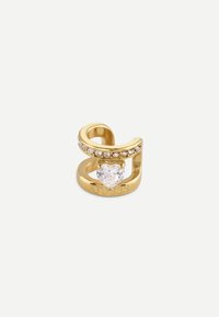Anello color oro con un design vorticoso, adornato con piccoli strass trasparenti e una pietra trasparente a forma di cuore al centro. Marcato "GUESS."