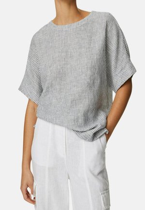 Femme portant un haut à manches courtes rayé verticalement gris et blanc, associé à un pantalon en lin blanc taille haute avec une poche latérale.