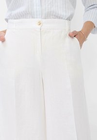 Pantaloni bianchi in lino con design dritto, caratterizzati da chiusura con bottone, tasche laterali e una superficie liscia, leggermente testurizzata.