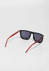 Ochelari de soare negri cu lentile violet și brațe din cauciuc roșu. Design cu ramă rectangulară și finisaj strălucitor, cu balamale vizibile.