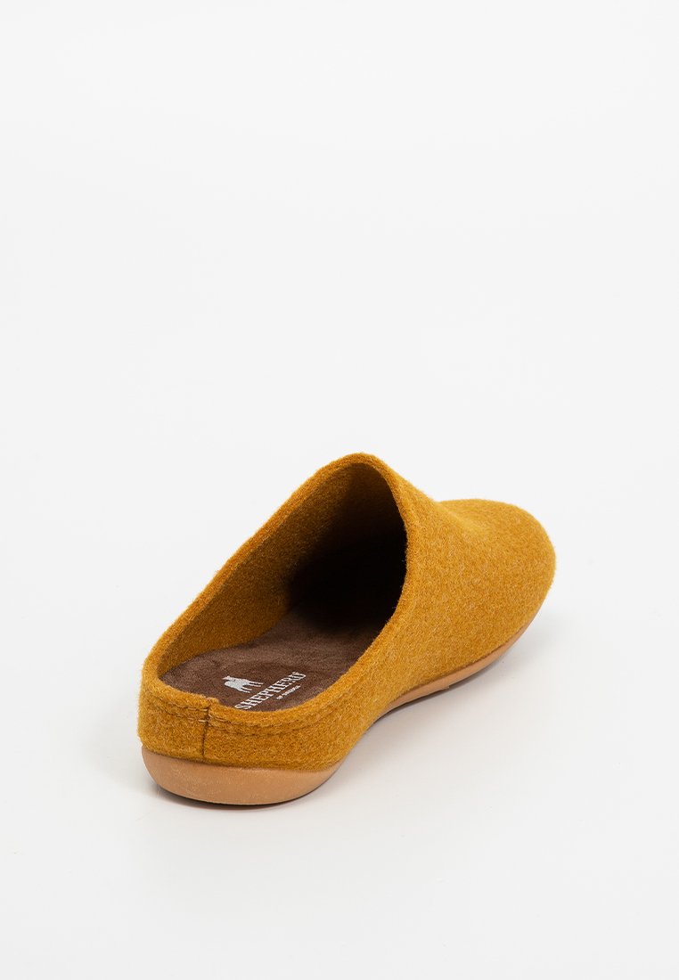 Ein einzelner senfgelber Slipper zum Hineinschlüpfen mit einem weichen Stoffobermaterial und einer braunen gepolsterten Innensohle auf einem hellen Hintergrund.