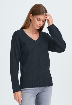 Pull en maille côtelée gris foncé avec un col en V, des manches longues et une coupe décontractée, associé à un jean gris clair.