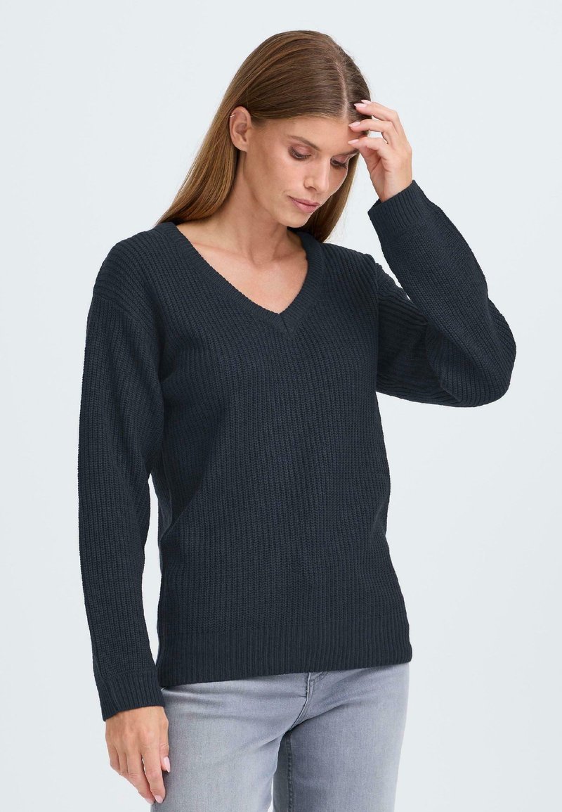 Mörkgrå, ribbad stickad tröja med V-hals, långa ärmar och en avslappnad passform, tillsammans med ljusgrå jeans.