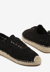 Chaussures en dentelle noires avec un motif floral texturé, semelle en corde de jute et capuchon beige, dotées d'œillets pour les lacets et d'une tige basse.