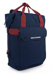 Mochila de lona azul marino con correas rojas, un bolsillo frontal y un cierre en la parte superior. Presenta una estructura firme y detalles de herrajes en contraste.