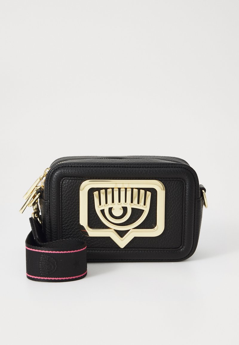 Borsa a tracolla in pelle nera con un prominente emblema dorato a forma di occhio. Presenta una tracolla rimovibile con accento rosa e superficie testurizzata.